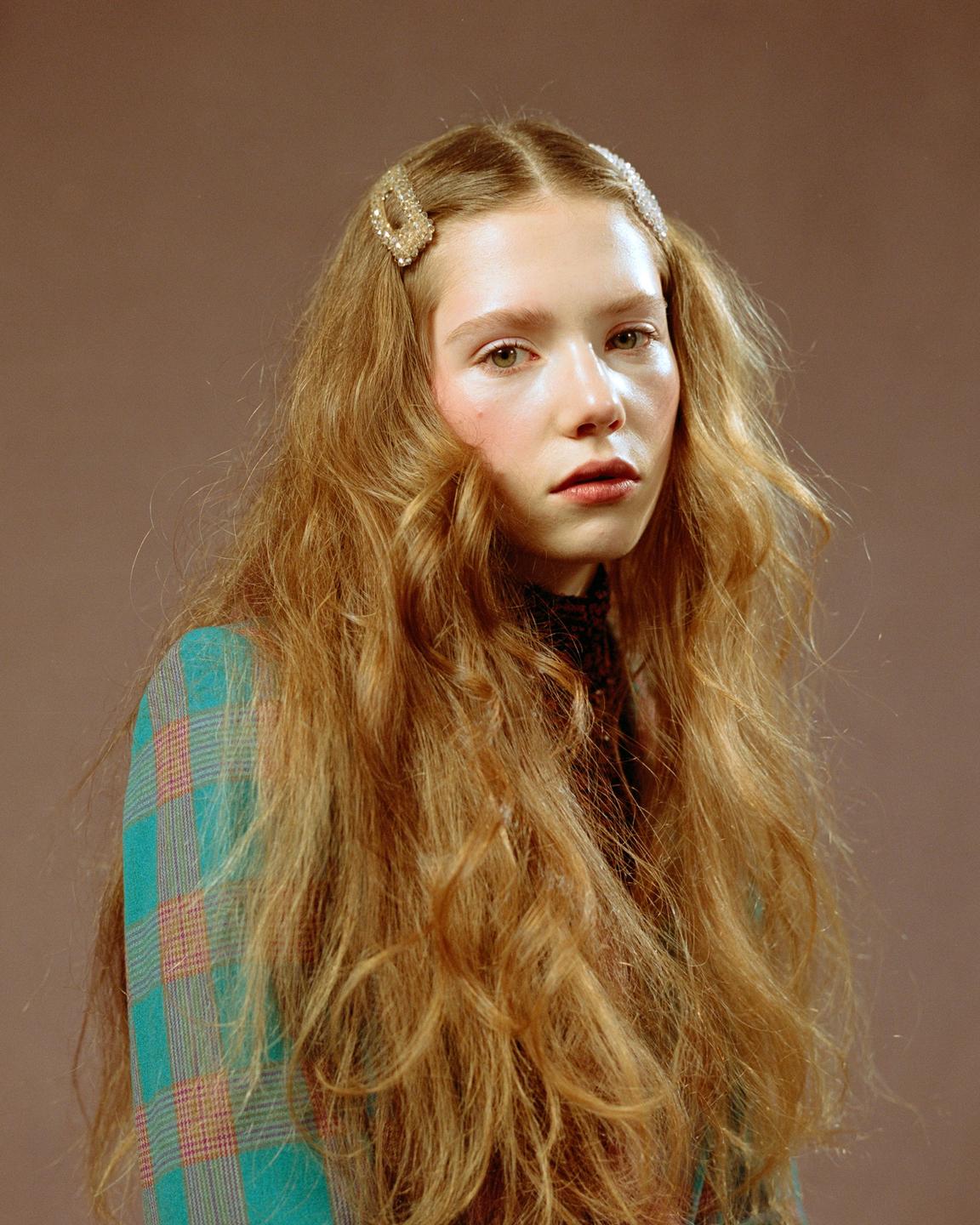 A woman with long, wavy hair and two hair clips looks directly at the viewer.