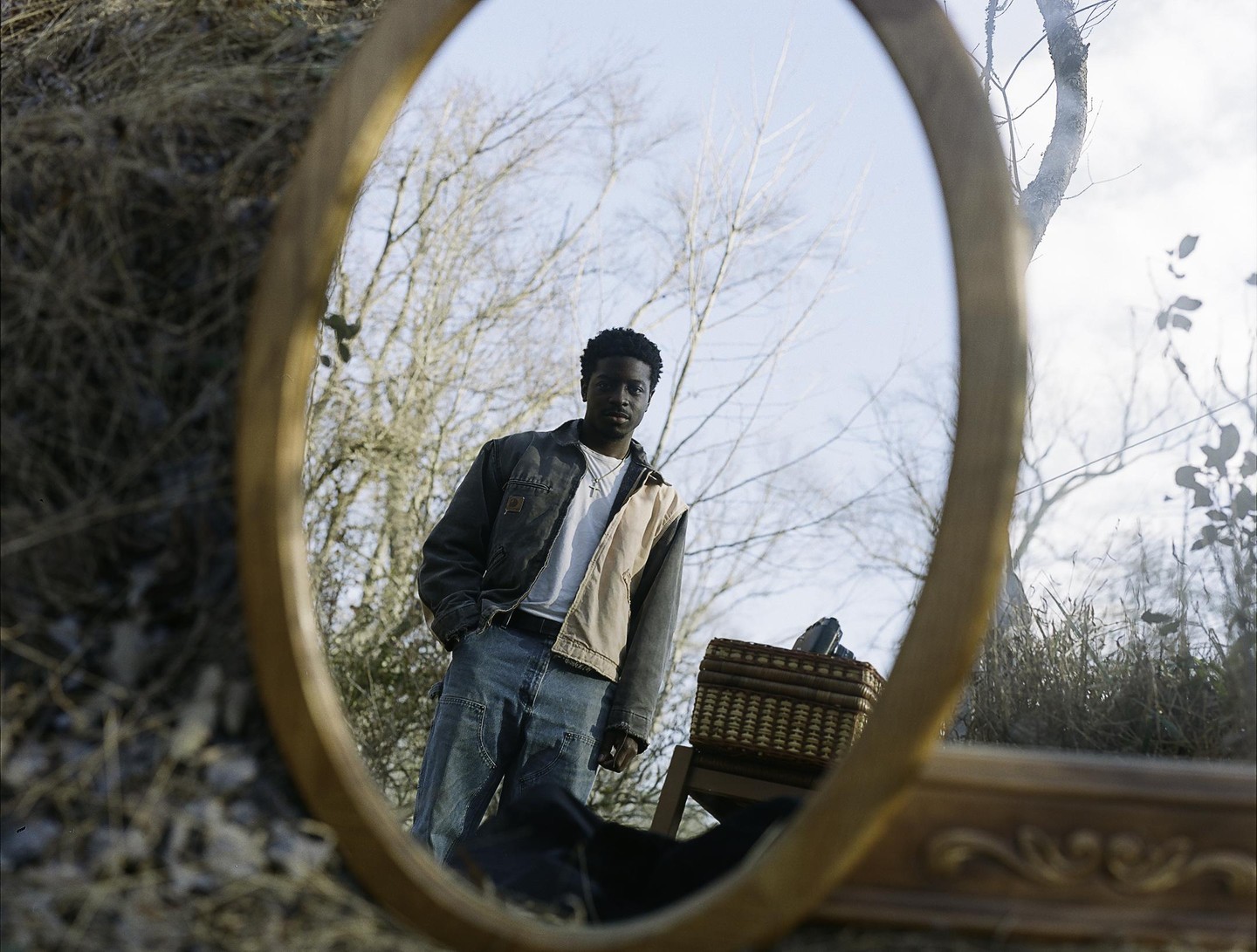 A man is reflected in an oval mirror placed on the ground in a forest.