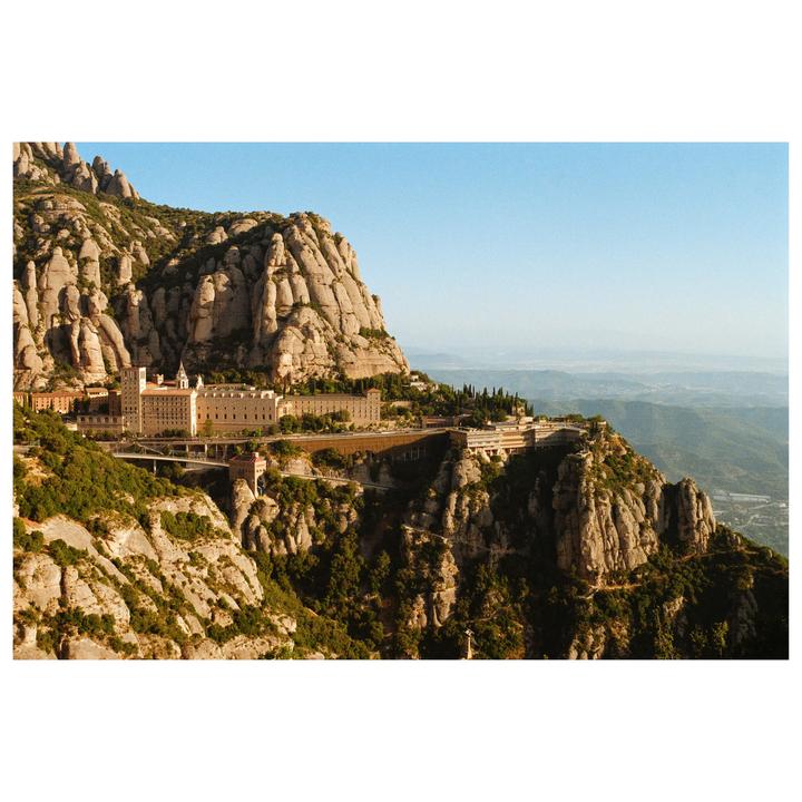 A large monastery complex is built into the side of a rocky mountain under a clear sky.
