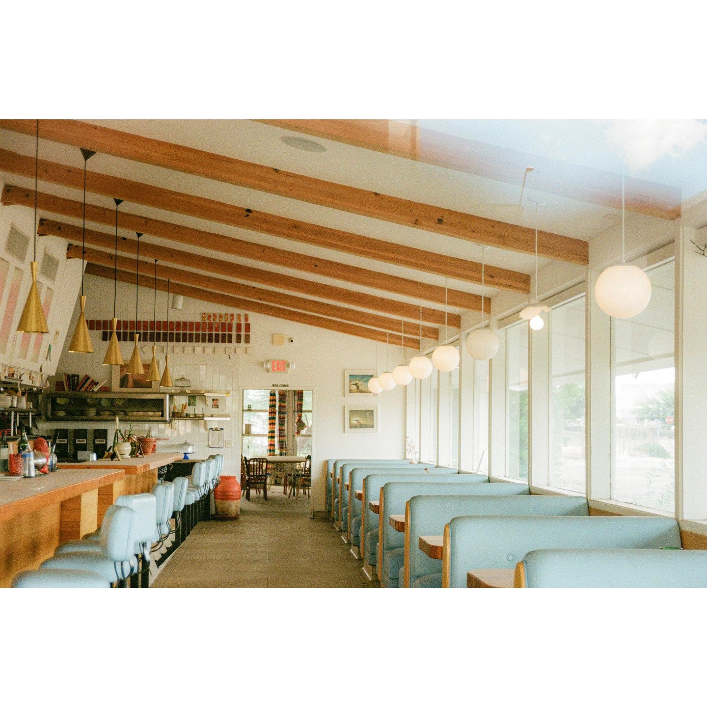 A diner interior features a counter with stools and a row of booths next to large windows.