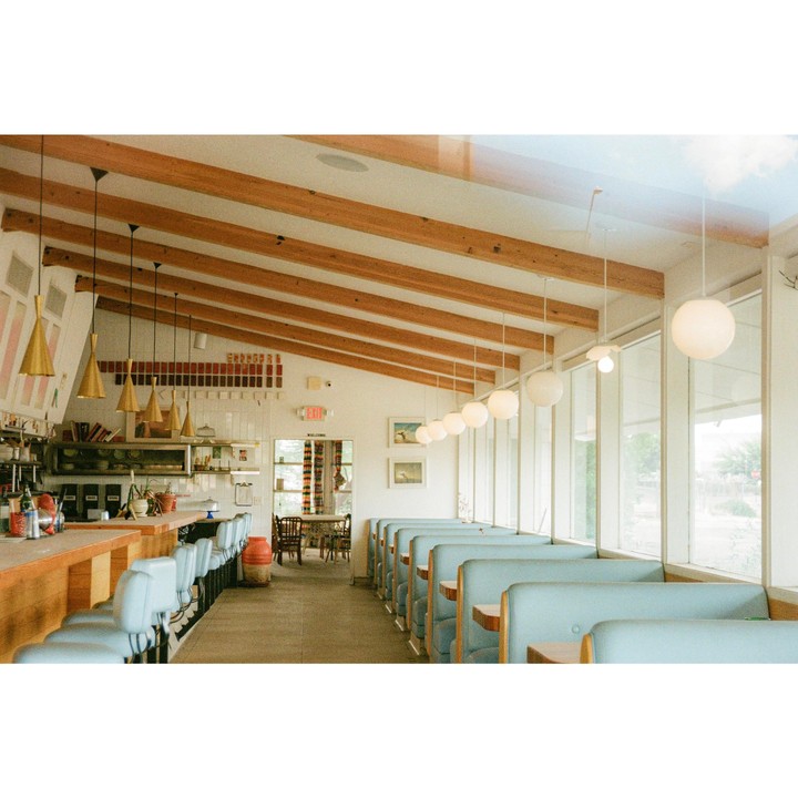 A diner interior features a counter with stools and a row of booths next to large windows.
