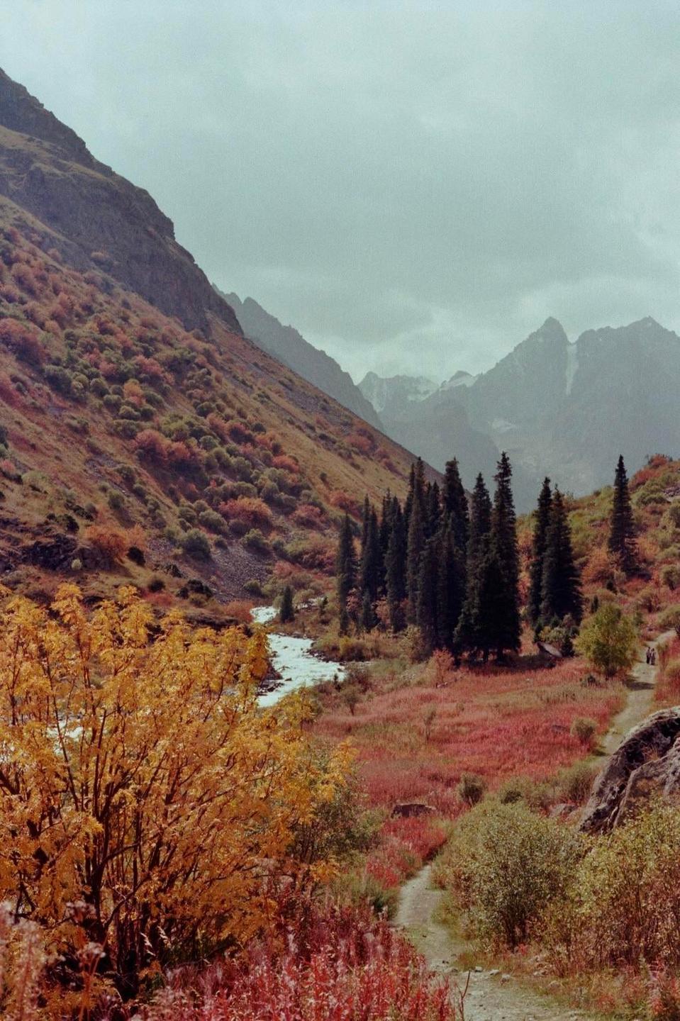 A river flows through a valley with mountains and colorful autumn foliage.