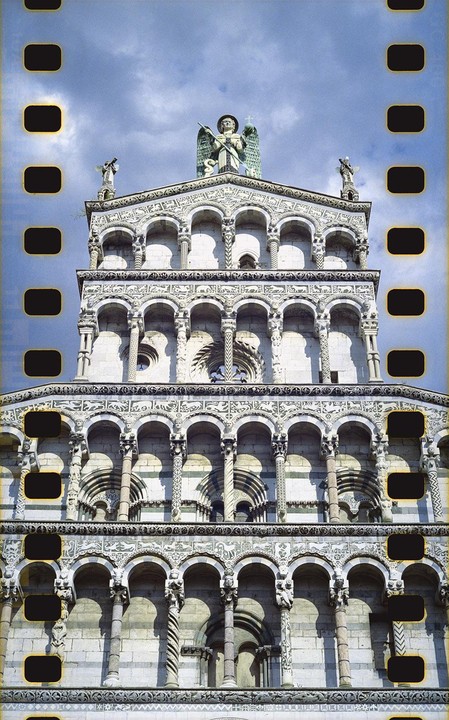 A detailed view of an ornate church facade with multiple arches and statues under a cloudy sky.