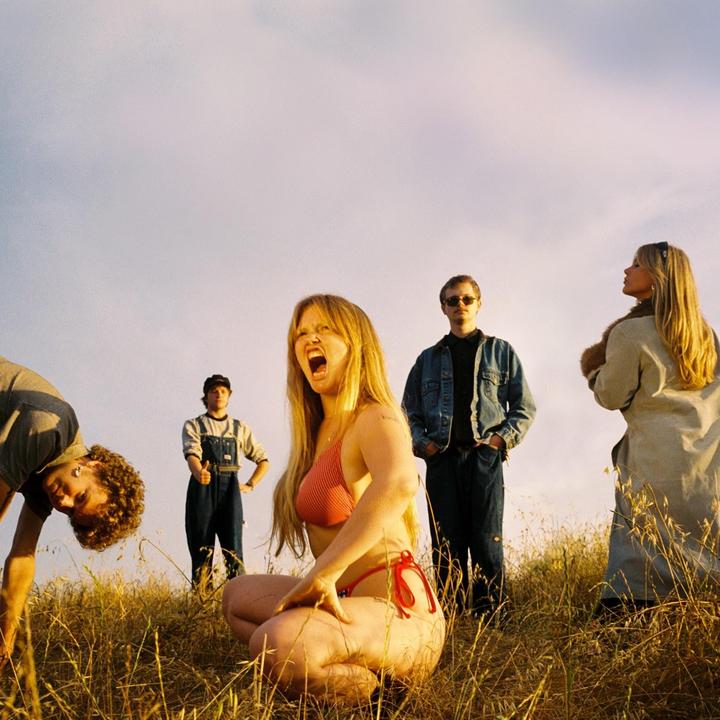 Five people are posing in a field of tall grass under a bright sky.