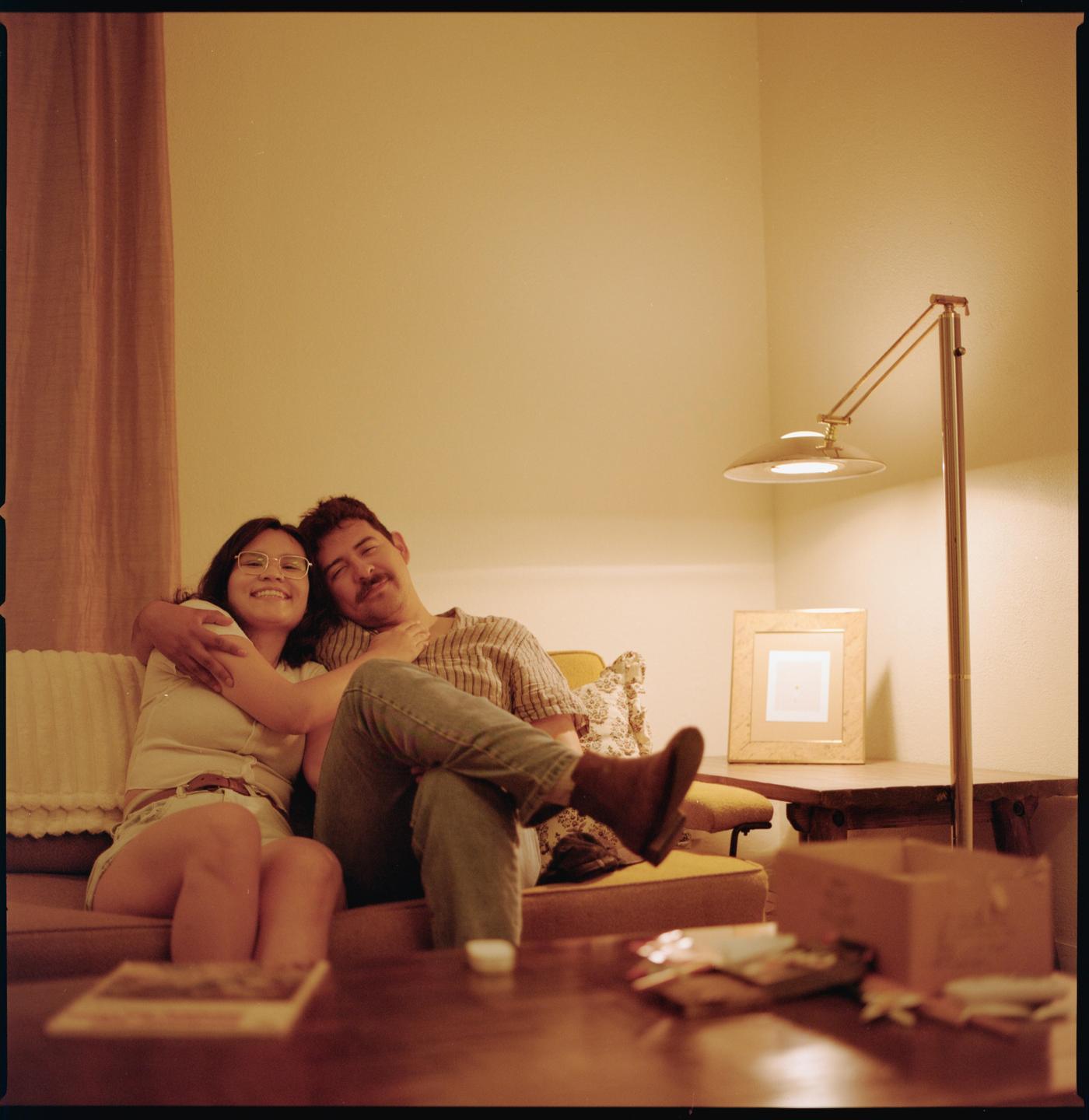 A couple is sitting on a sofa in a living room with a lamp and a coffee table.