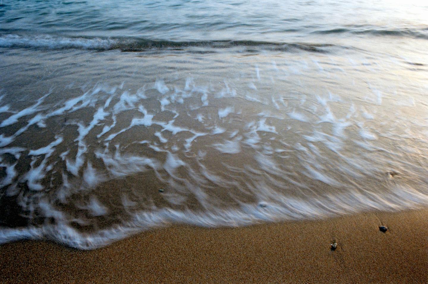 A wave washes over a sandy beach, leaving foamy patterns on the wet sand.