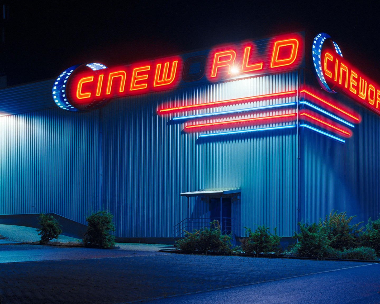 A Cineworld cinema building is illuminated by red and blue neon lights at night.