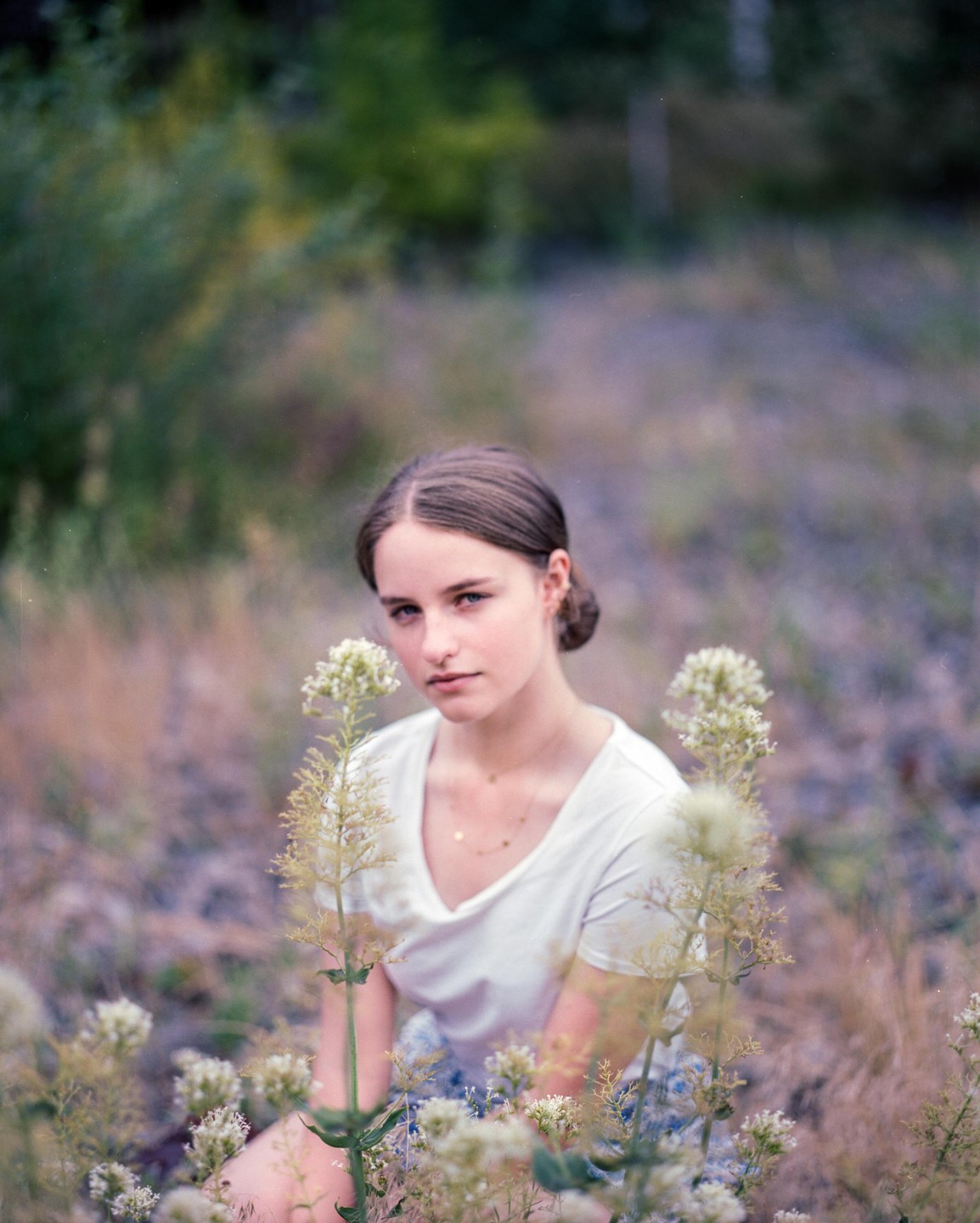 A woman sits in a field of wildflowers, looking directly at the viewer.