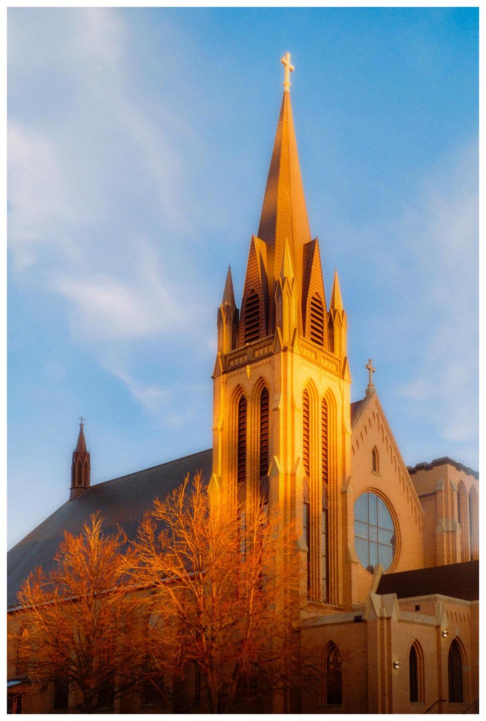 A church with a tall steeple is illuminated by golden light against a blue sky.