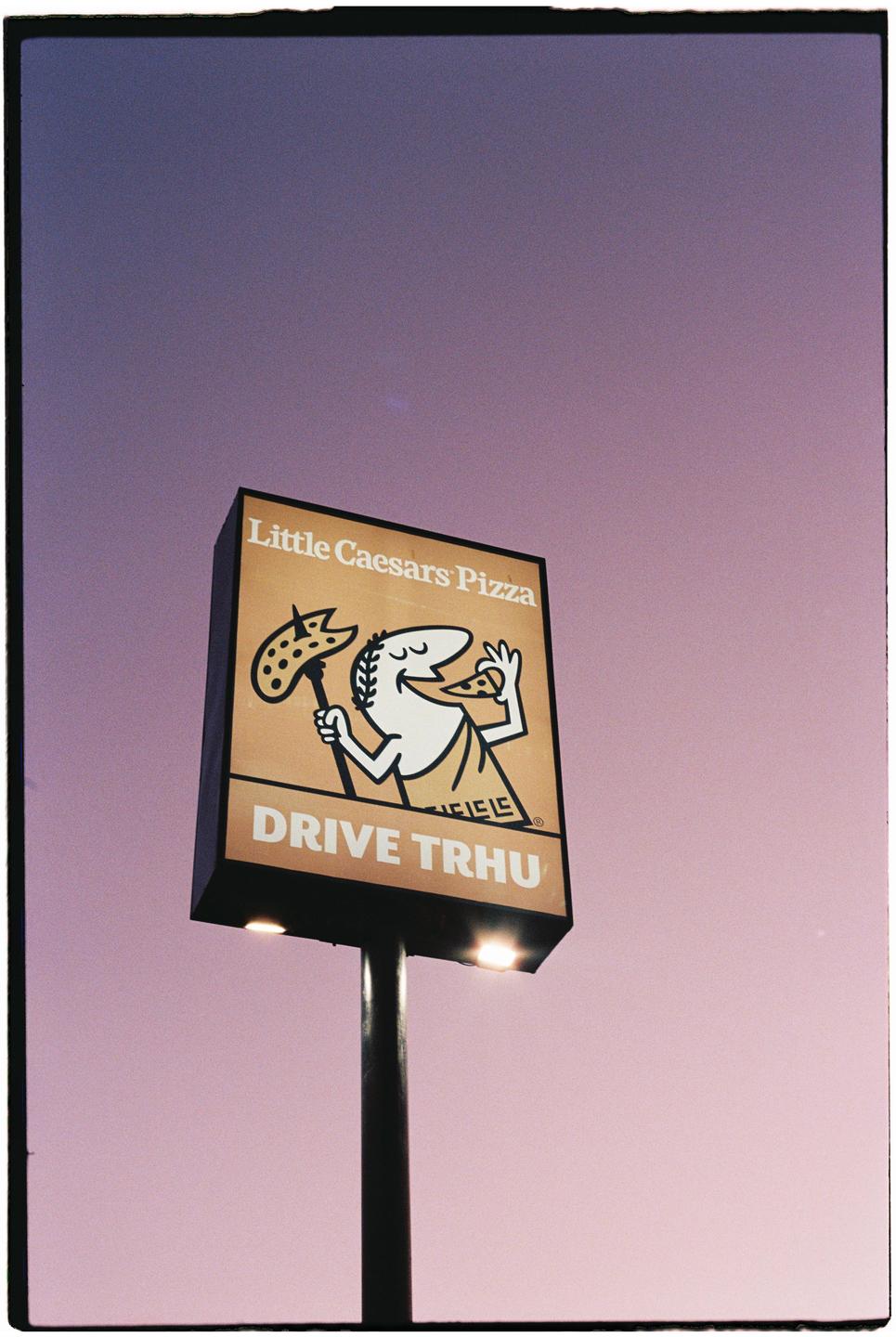 A Little Caesars Pizza drive-thru sign is illuminated against a purple sky.