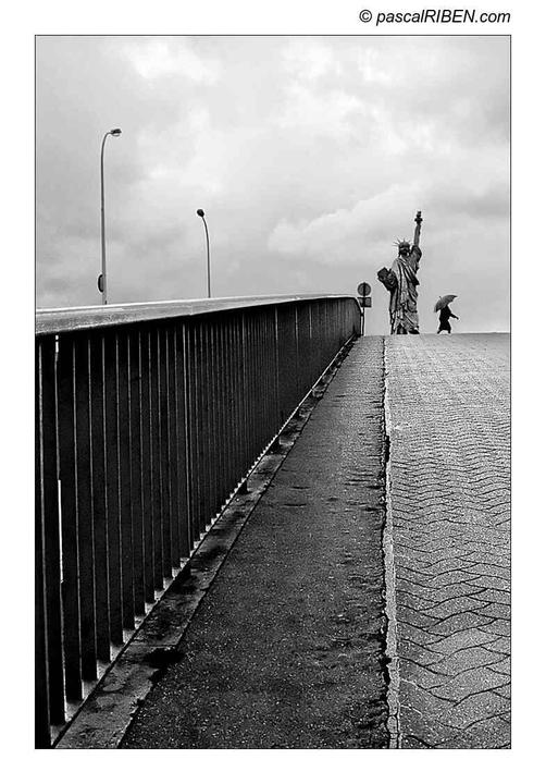A person with an umbrella walks past a replica of the Statue of Liberty on a bridge in Paris.