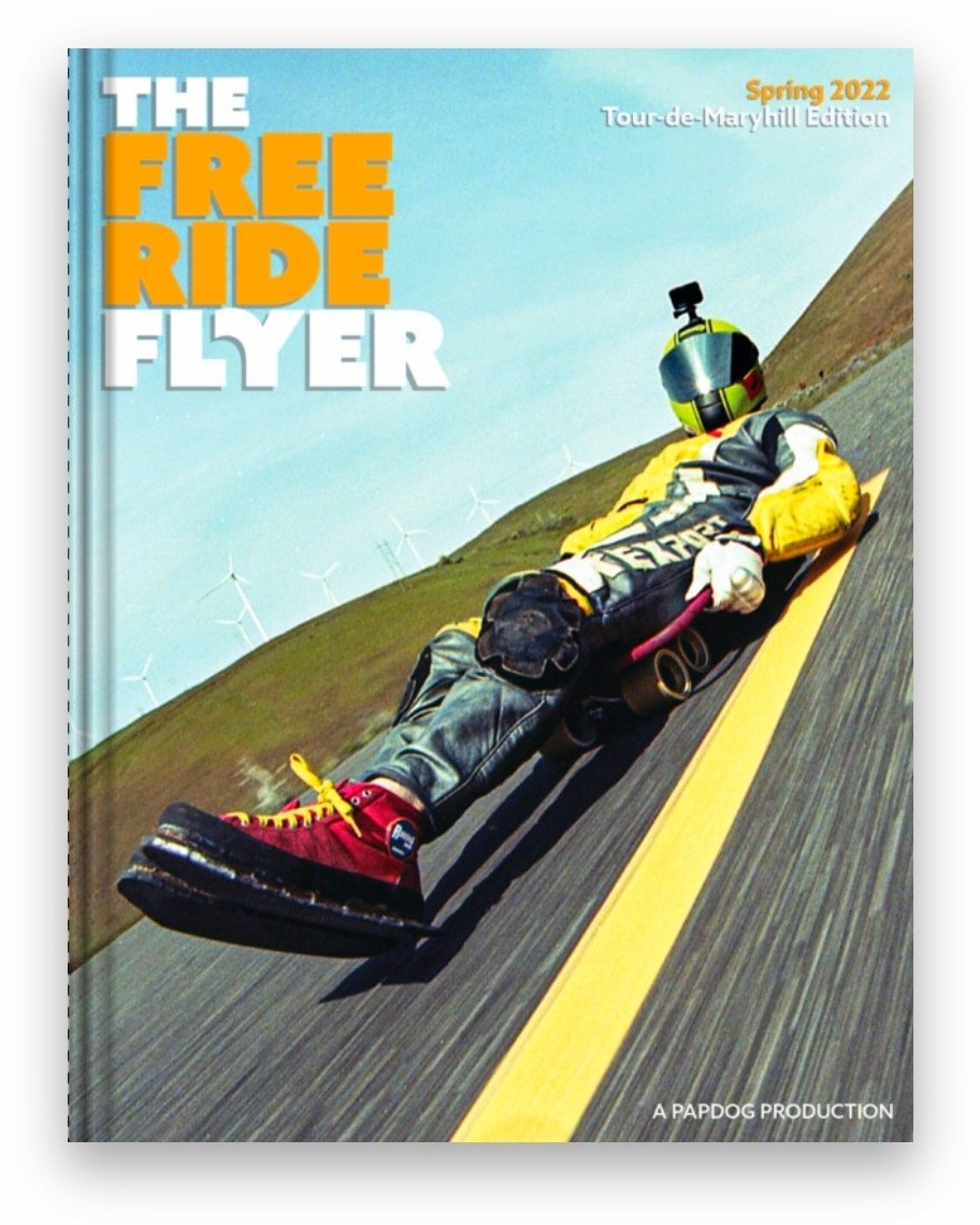 A person in a helmet and protective gear is riding a street luge down a paved road with a yellow line.