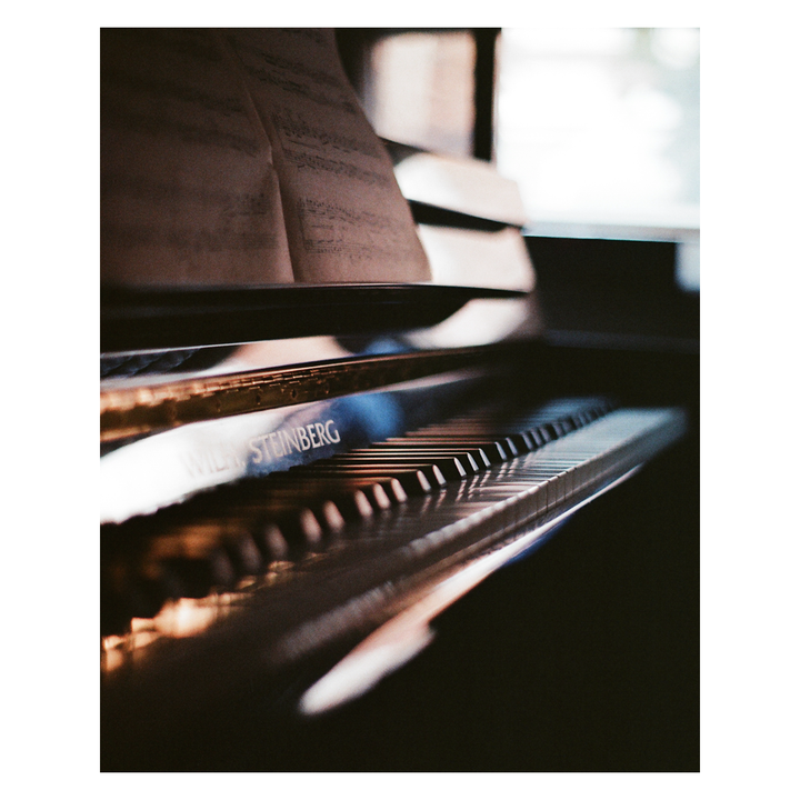 A close-up shot shows the keys and music stand of a piano with sheet music on it.