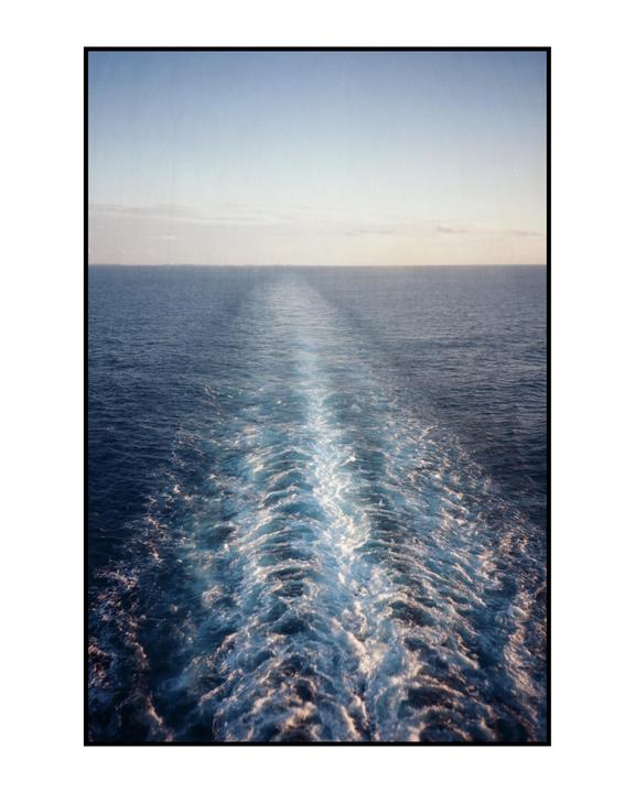 A boat's wake trails across the ocean under a clear sky.