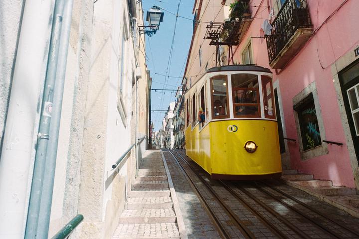 A yellow tram ascends a steep, narrow street lined with buildings in Lisbon.