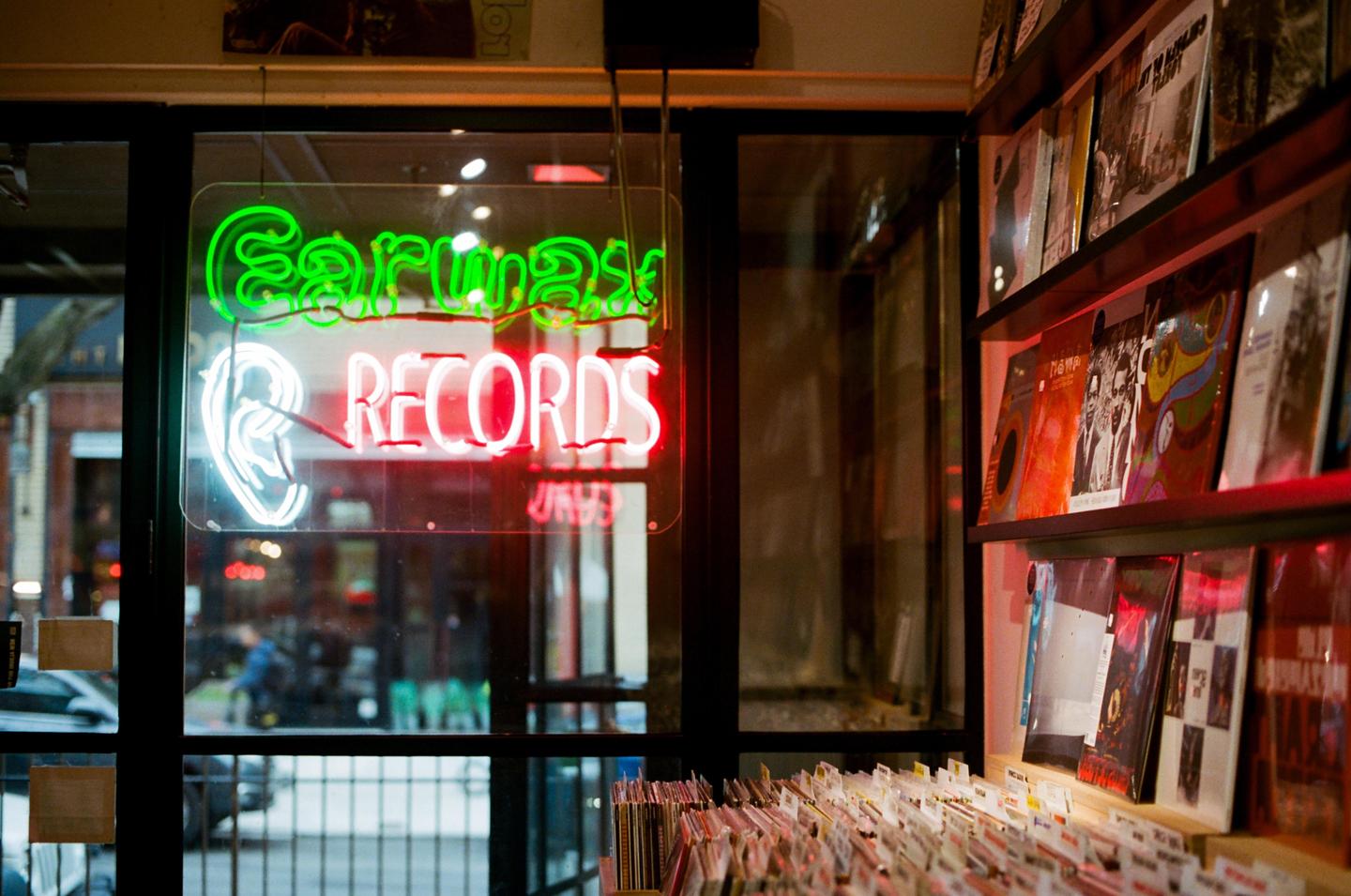 A neon sign for "Earwax Records" is visible through a window, with records displayed on shelves inside.