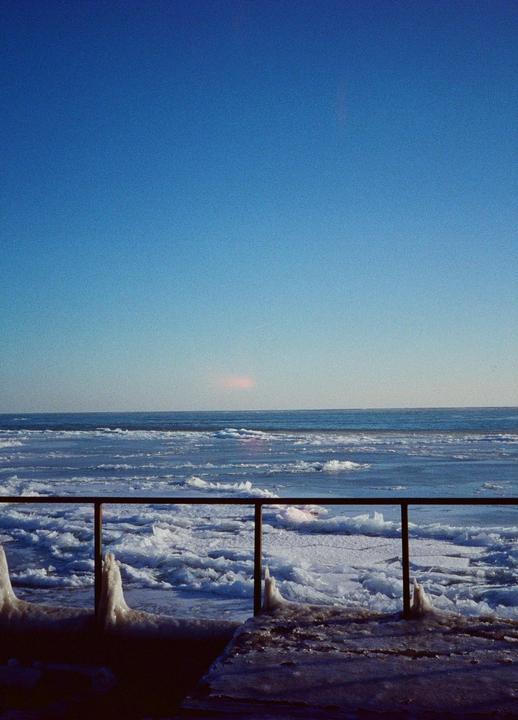A metal railing covered in ice overlooks a frozen lake under a clear blue sky.