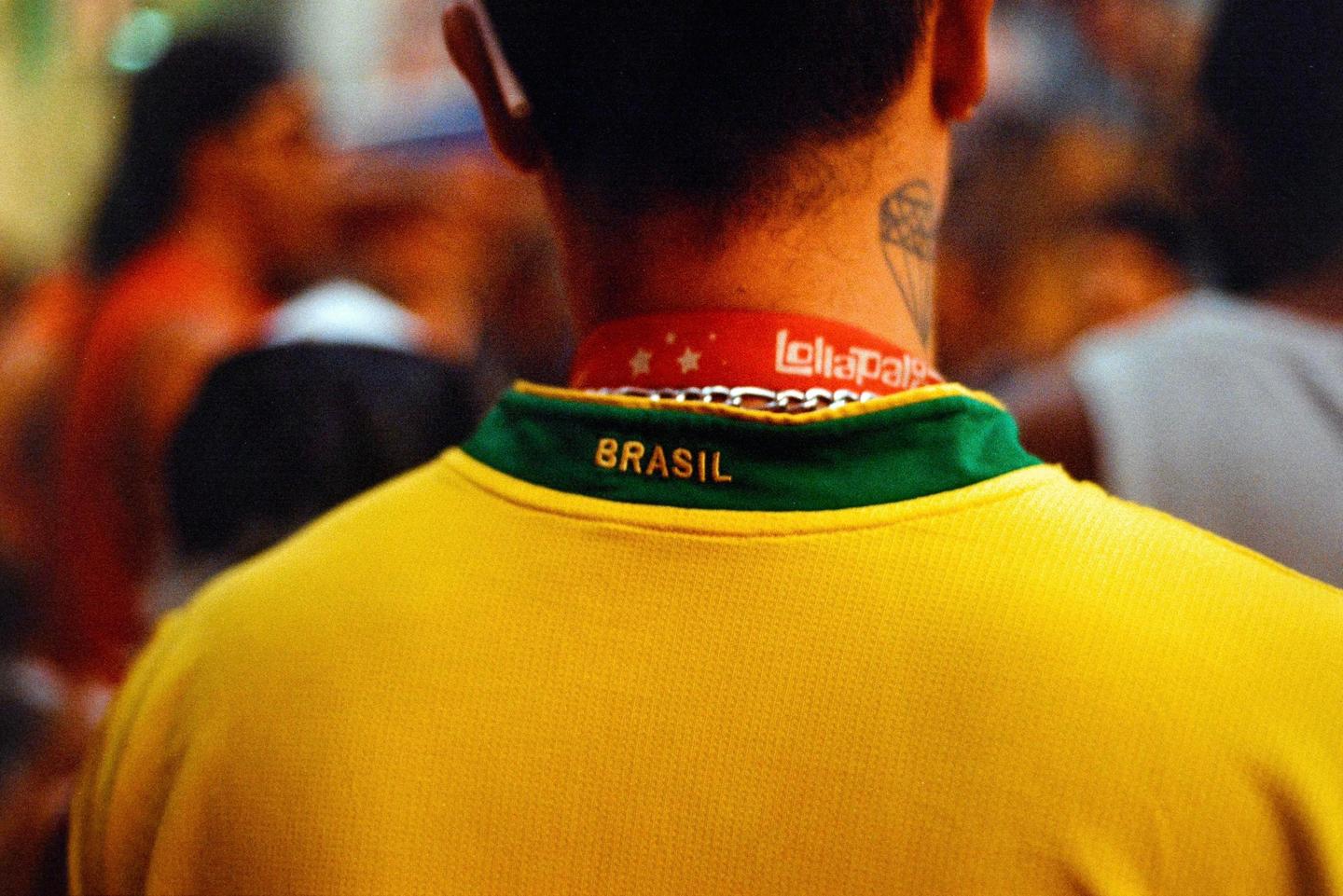 A person wearing a yellow and green shirt with "BRASIL" written on the collar is seen from behind, with a red lanyard around their neck.