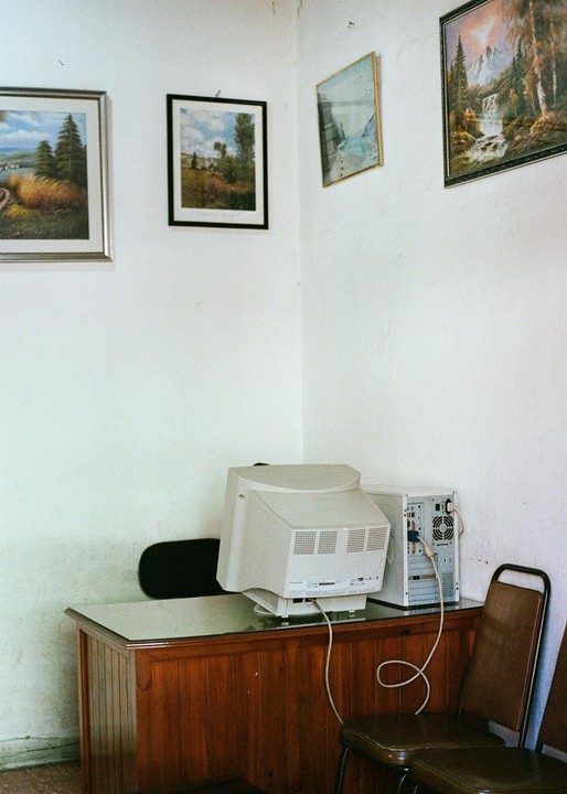 A desktop computer and monitor sit on a wooden desk with three framed pictures hanging on the white wall above.