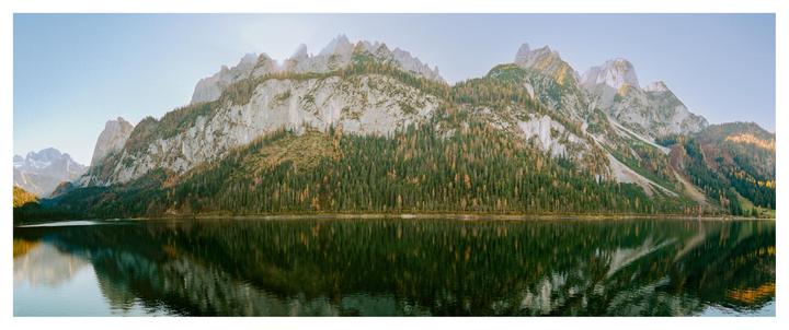 A panoramic landscape shows a mountain range covered in trees reflected in a still lake.