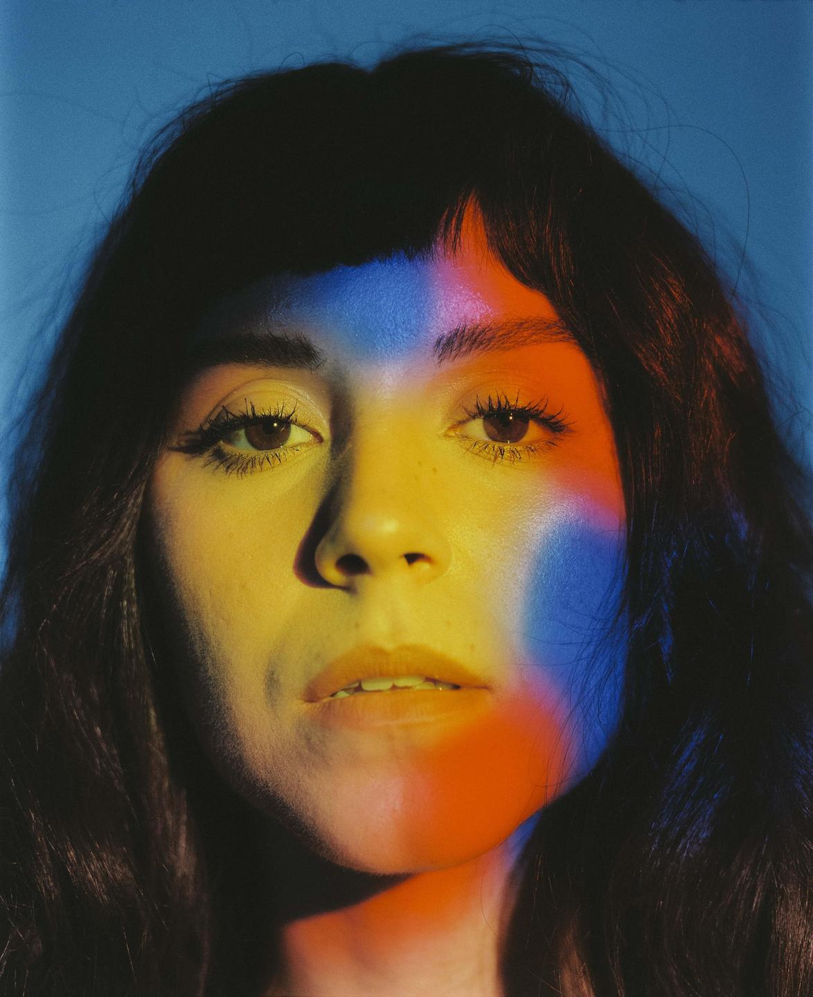 A woman's face is illuminated by blue, yellow, and red light.