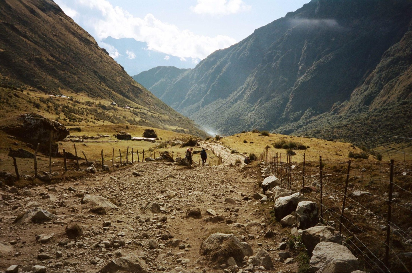 Three people walk down a rocky path between two mountains.