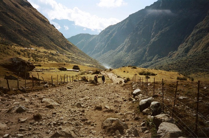 Three people walk down a rocky path between two mountains.