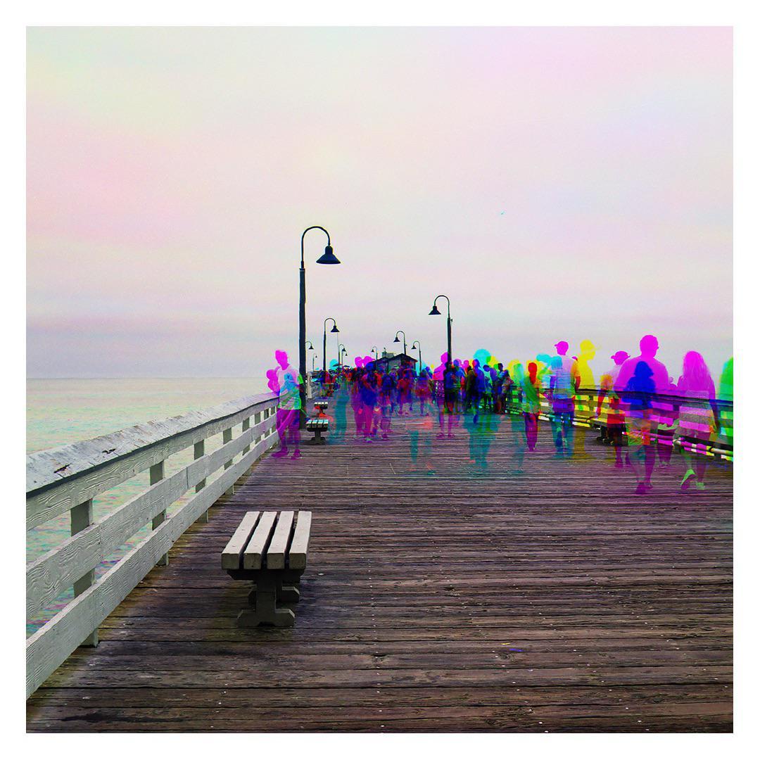A crowd of people with colorful, ghost-like outlines walks along a wooden pier next to the ocean.