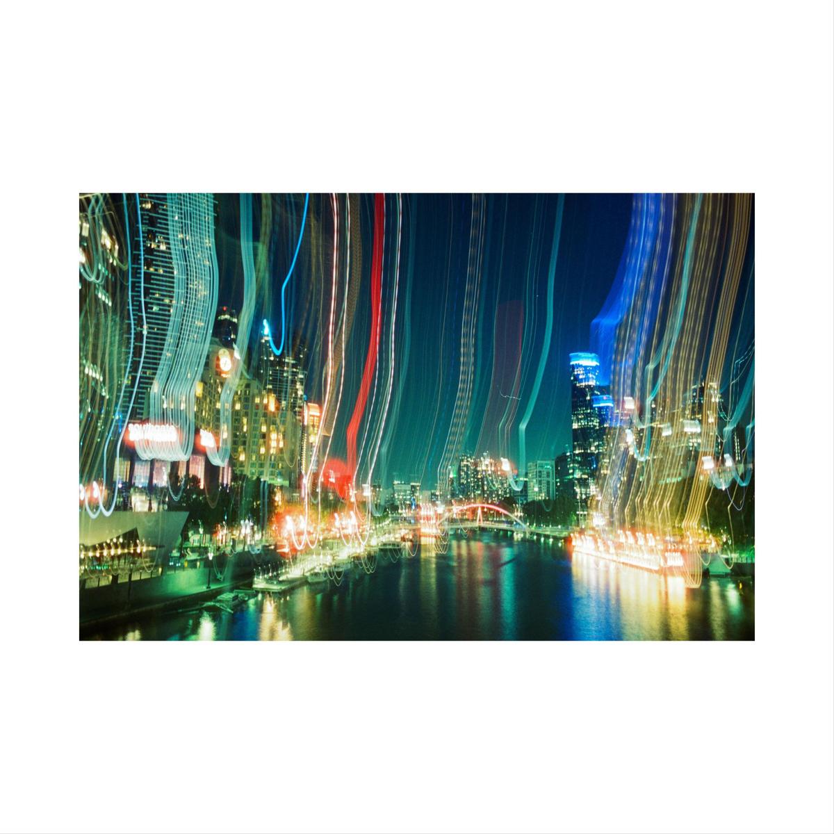 A long exposure photograph captures the light trails of a city at night, with buildings and a river visible.