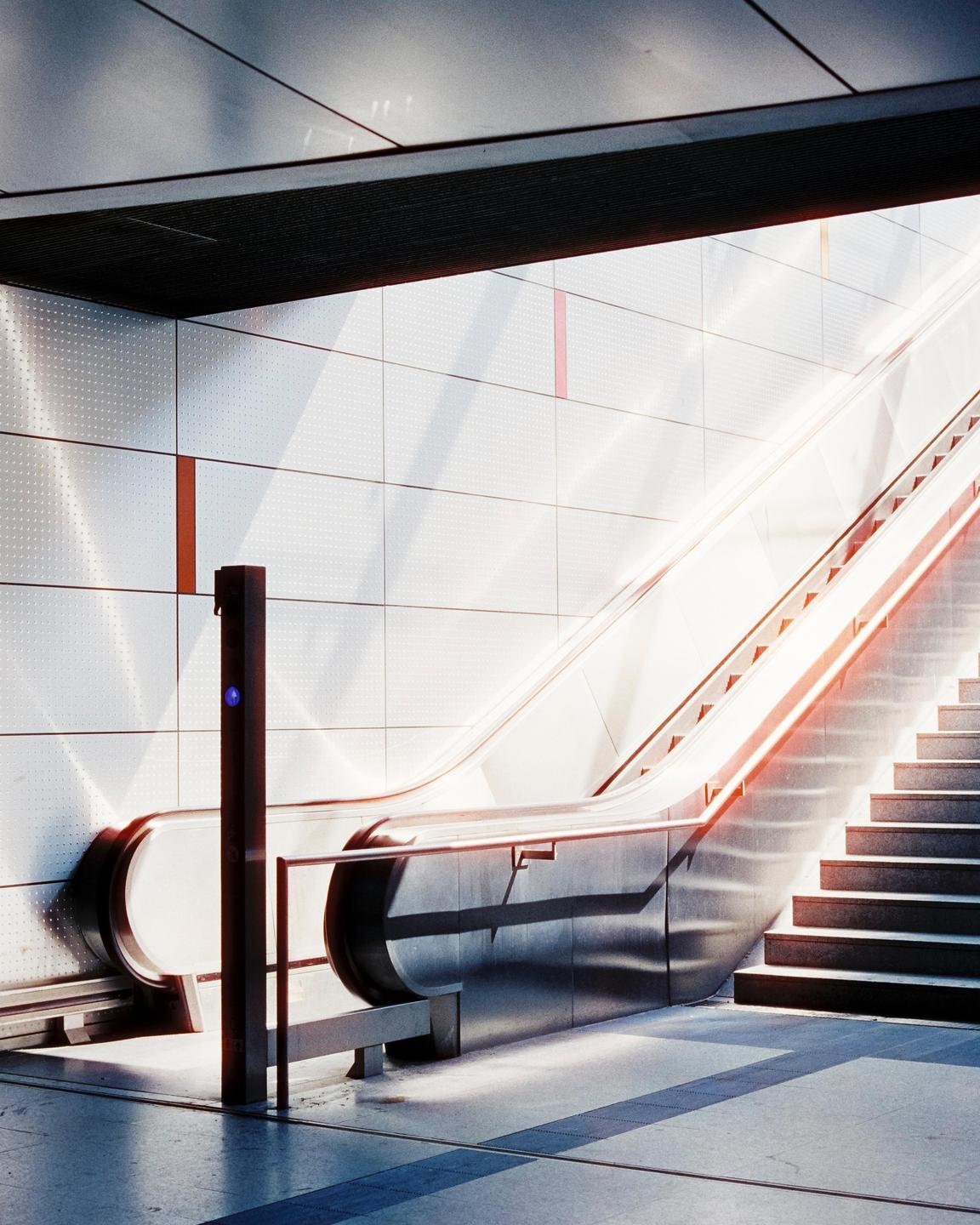 Sunlight illuminates an escalator and a staircase in a modern building.