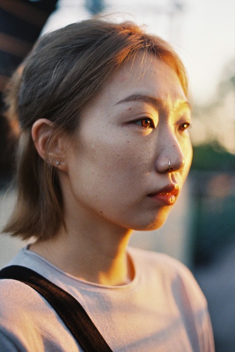 A woman with a nose ring is illuminated by golden light on her face and hair.