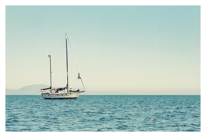 A sailboat floats on the water with mountains in the distance under a clear sky.