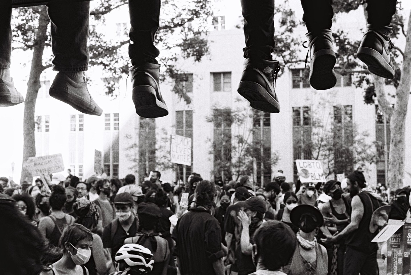 Several pairs of legs dangle above a crowd of people at a Black Lives Matter protest.