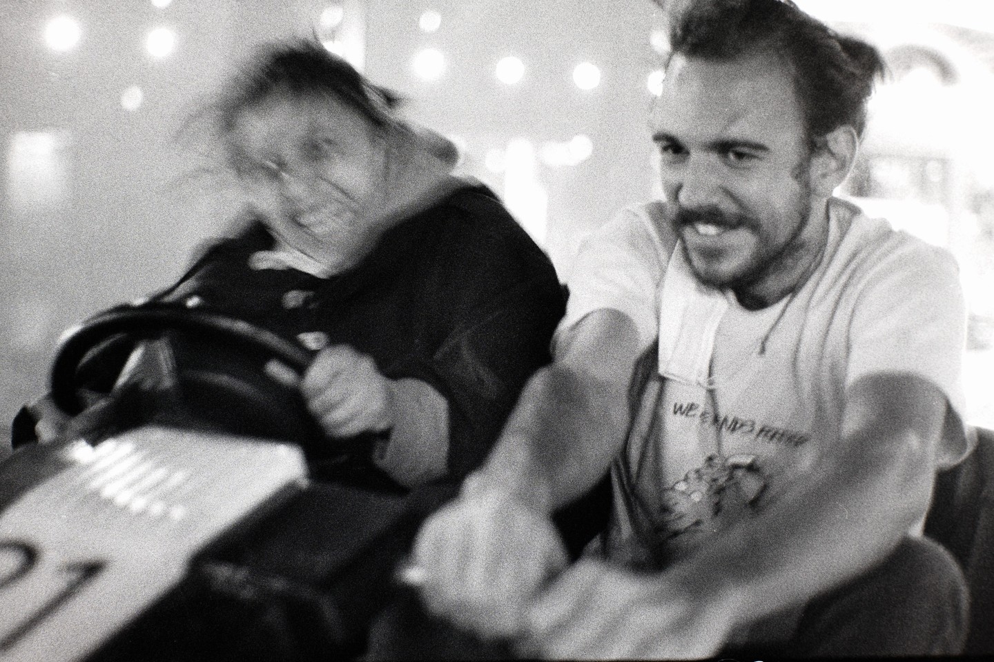 A man and a woman are riding in a bumper car, with the woman's face blurred from motion.