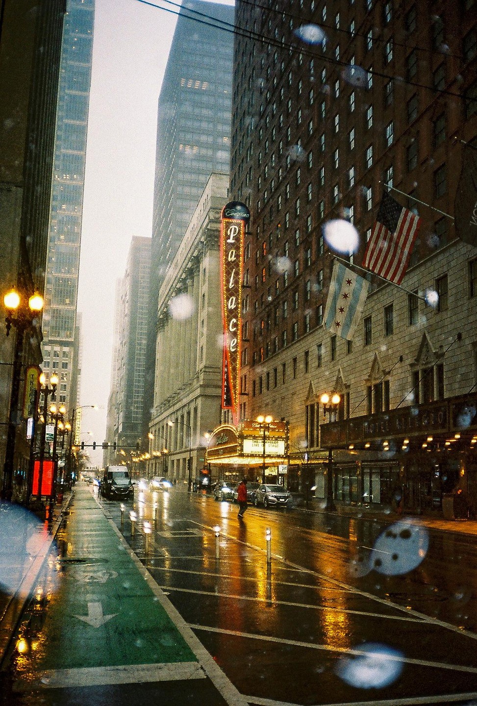 A street in a city is wet from rain, with a large theater marquee visible on the right.