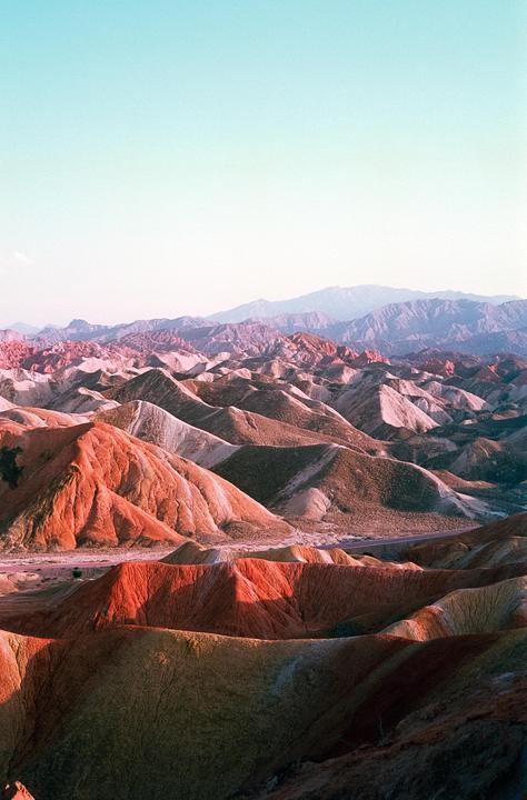 A vast landscape of colorful, undulating hills and mountains stretches under a clear sky.