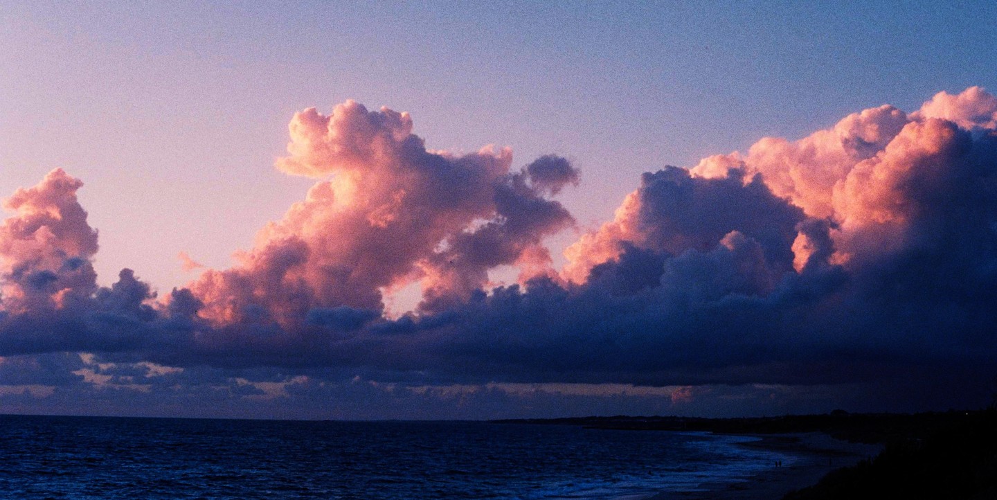 Pink and purple clouds hang over a dark ocean and beach at dusk.