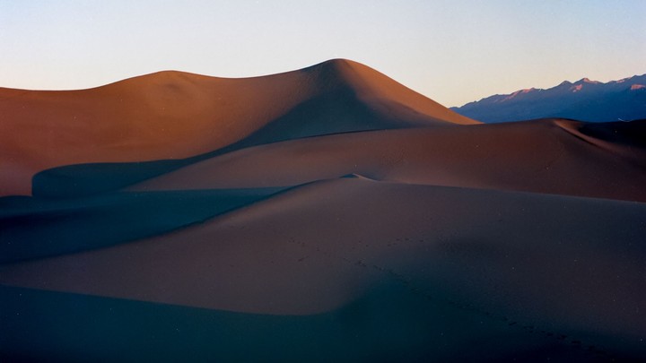 Sand dunes are illuminated by the setting sun, casting long shadows across the desert landscape.