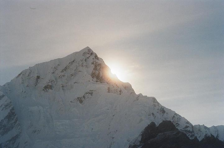 The sun shines brightly from behind a snow-covered mountain peak.