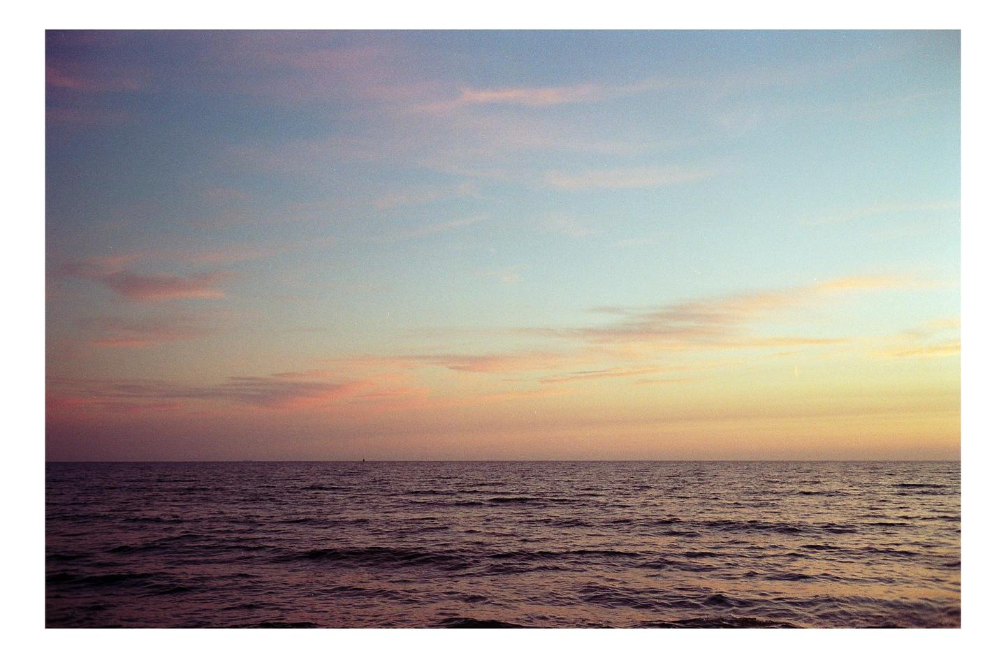 The ocean stretches to the horizon under a colorful sky at dusk.