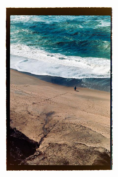 A person walks along a sandy beach next to the ocean with waves crashing on the shore.
