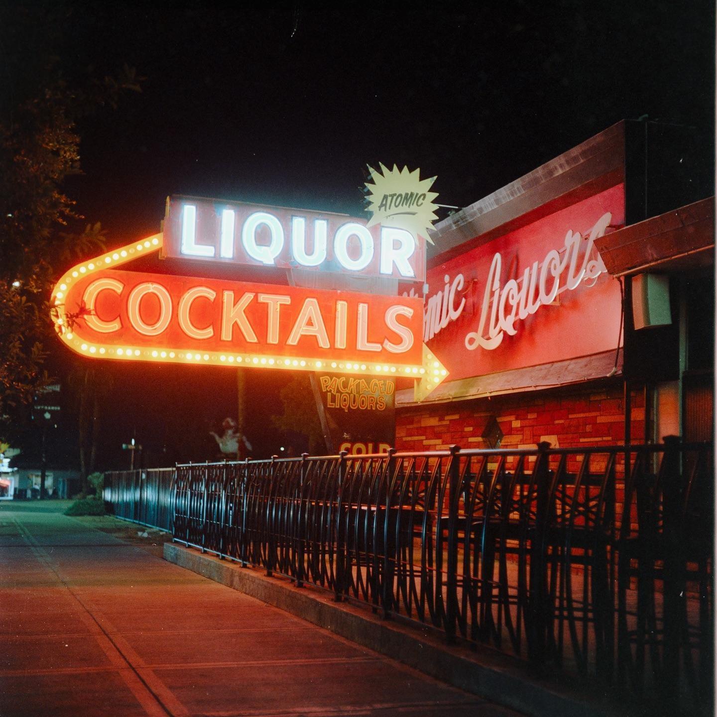 A neon sign for liquor and cocktails illuminates a building at night.