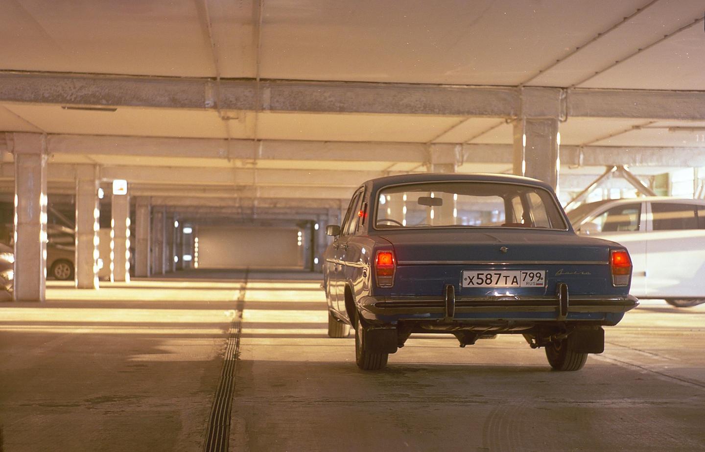 A blue car is parked in an underground parking garage with warm lighting.