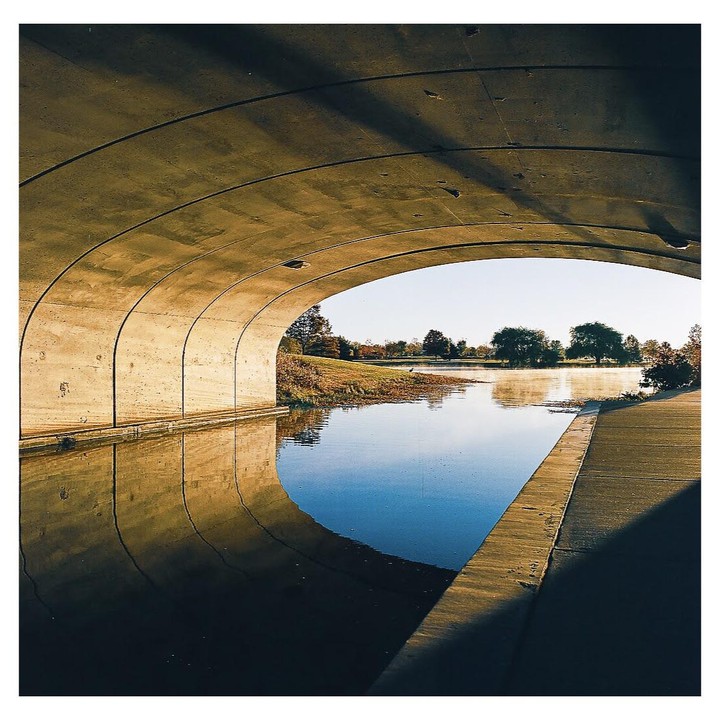 A concrete archway frames a body of water with trees on the far bank under a clear sky.