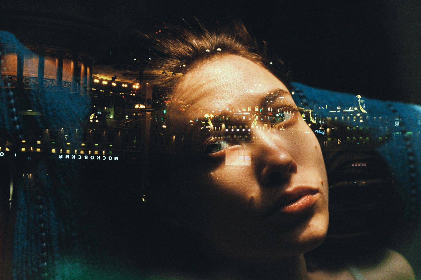 A woman's face is superimposed over a night cityscape with illuminated buildings and a river.