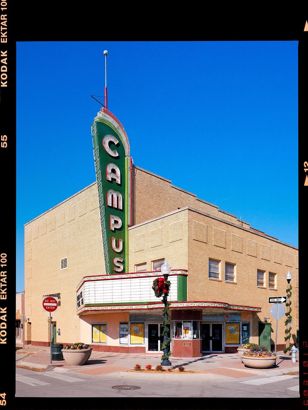 A vintage movie theater with a tall "CAMPUS" sign stands on a street corner under a clear blue sky.
