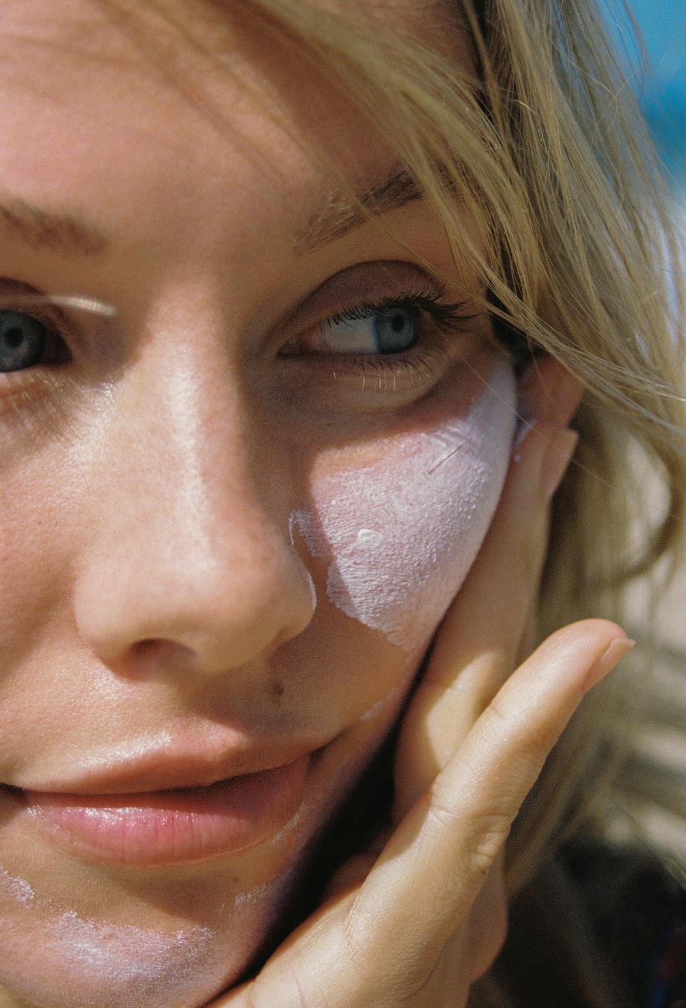 A woman applies sunscreen to her face.