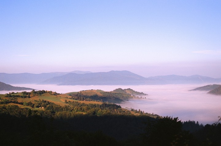 A valley filled with fog is surrounded by hills and mountains under a clear sky.