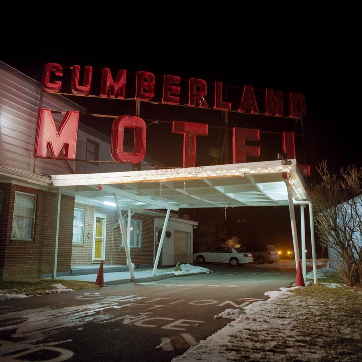 A red neon sign for the Cumberland Motel stands over a snowy driveway at night.