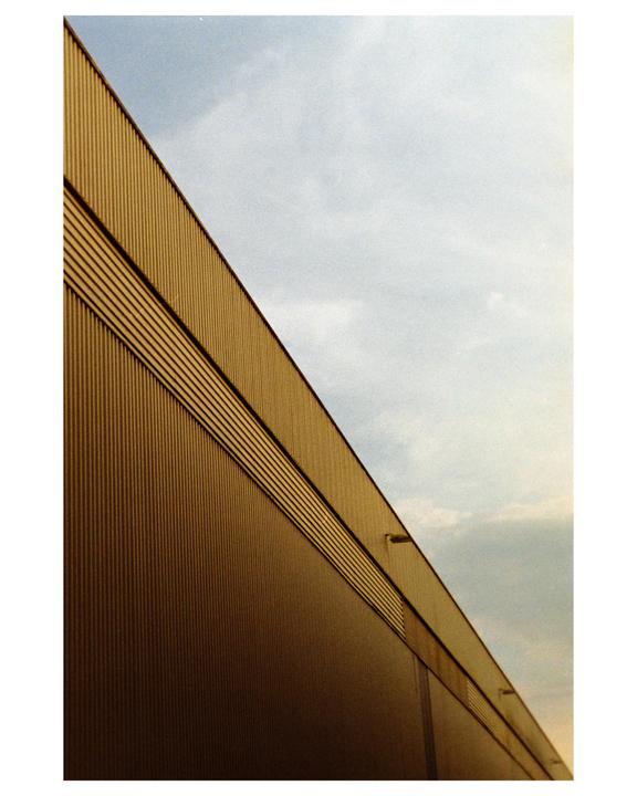 A corrugated metal building with a diagonal roofline is shown against a cloudy sky.